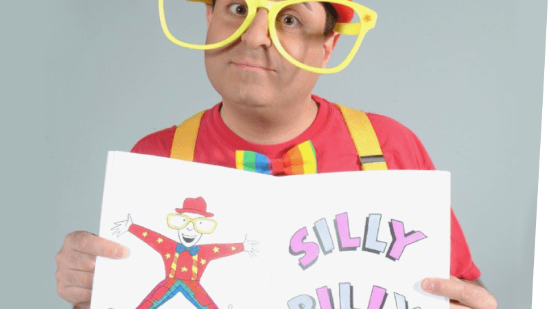 Silly Billy Magician wearing big yellow glasses and a red hat while holding a sign that reads "Silly Billy"