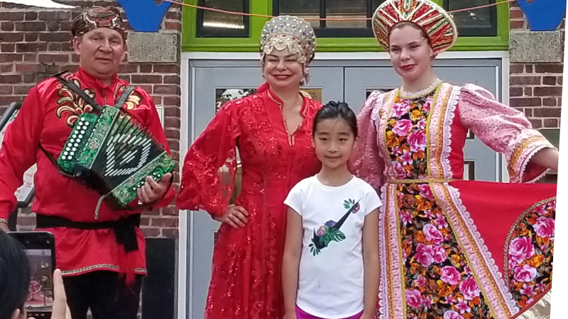 Performers wearing cultural attire posing for a picture with a smiling child in front of the children's museum.