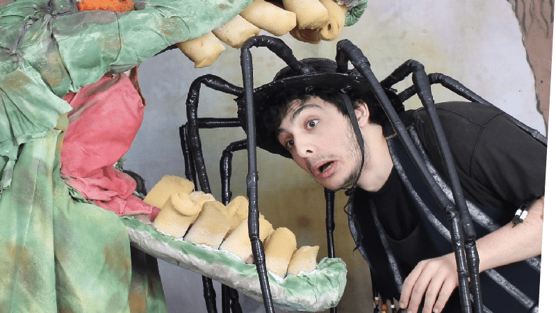 An actor dressed as a spider has his head between the jaws of a a costume crocodile