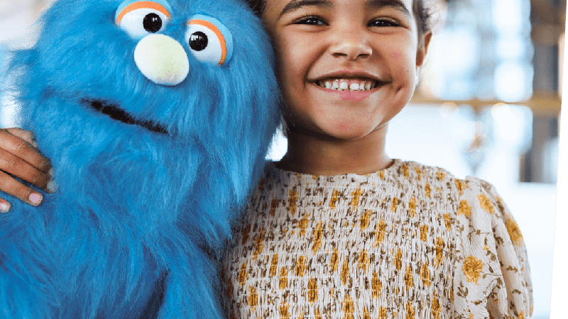 child smiling and hugging a blue monster like puppet