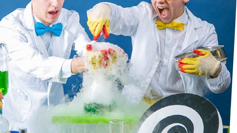 two young scientists with colorful bowties are astonished by what is emerging from a bubbling and seemingly steaming flask