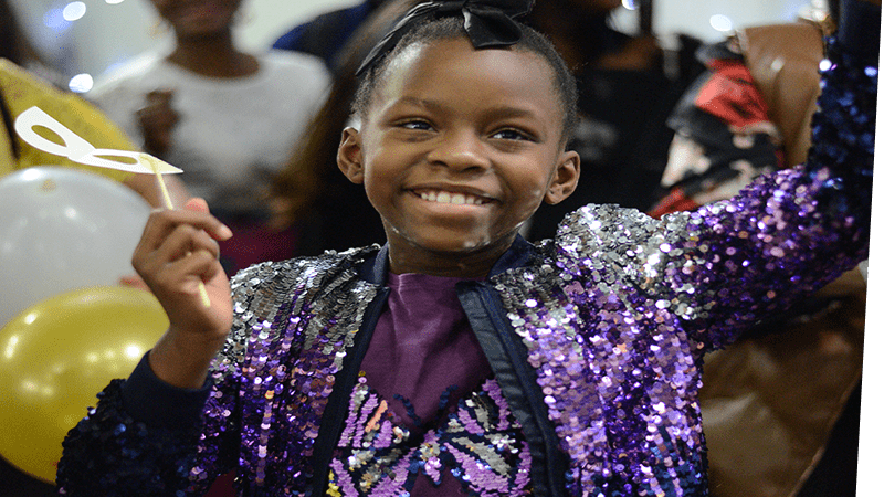 smiling child in a sparkly outfit in the midst of a baloon drop