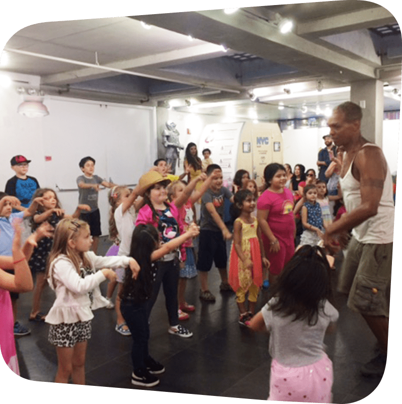 Several children surrounding Walter Rutledge while he teaches them dance moves