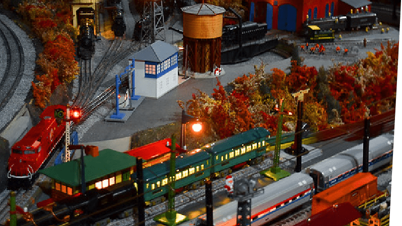 A model train village with trains in the station and the lamposts alight