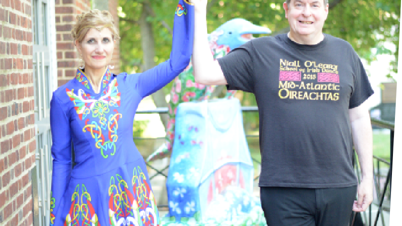 Woman and man Irish step dance performers hold hands aloft in a pair-dance stance.