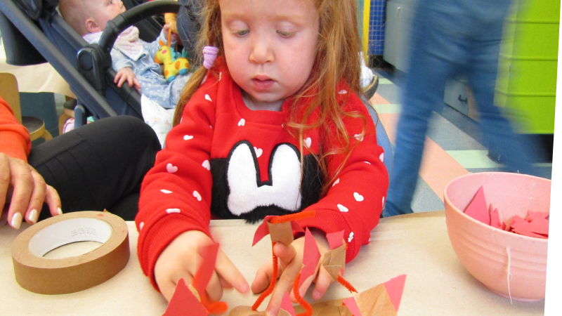 Child creating a sculpture with red pipe cleaners, construction paper and tape