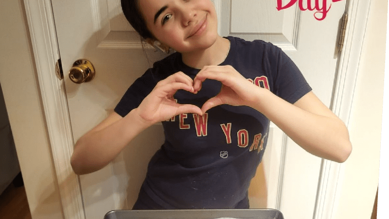 Maddison French making a heart shape with her hands, standing behind a try of freshly baked cookies